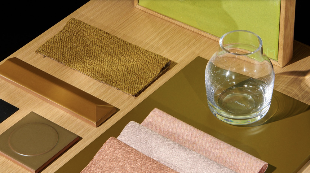 Materials in brown, shades of pink, beige and red on a light wood table. A glass vase stands to the right of the image on the same table.